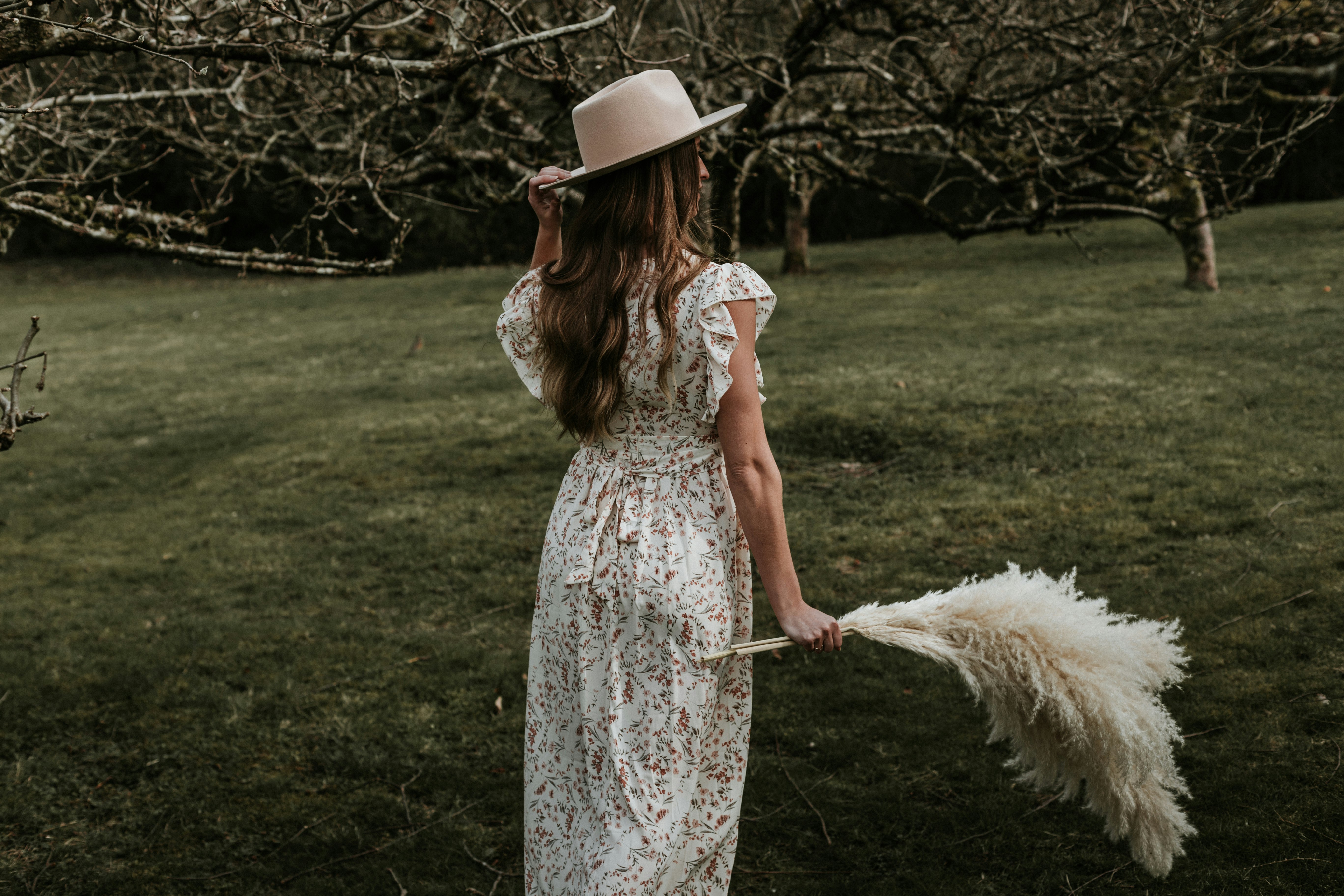 woman in white floral dress holding white umbrella standing on green grass field during daytime